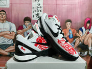 Angled view of white Nike basketball sneakers featuring black Swoosh branding, red graphics, black laces, and black midsoles.