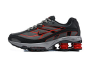 Side view of a black and grey Nike Shox Ride 2 sneaker with red accents and visible red cushioning columns.