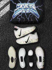 Off-white and black Nike sneakers shown with the patterned outsole, sole components, and a black lightning-themed box.