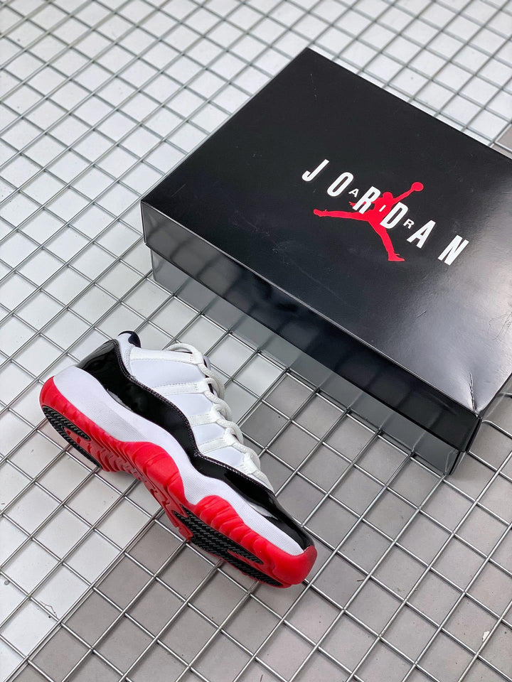 Air Jordan 11 sneaker shown beside a black Jordan shoe box, with black, white, and red color blocking.