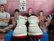 Front view of white adidas basketball-style sneakers with black details and red outsoles on a blue shoe box.
