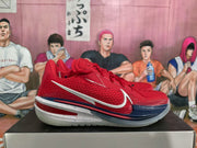 Side profile of a red Nike basketball sneaker showing the textured upper, white side branding, dark blue midsole accents, and translucent outsole.