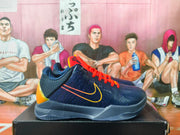Side view of a navy Nike Kobe basketball shoe with yellow side detailing, orange-red accents, and a gray outsole