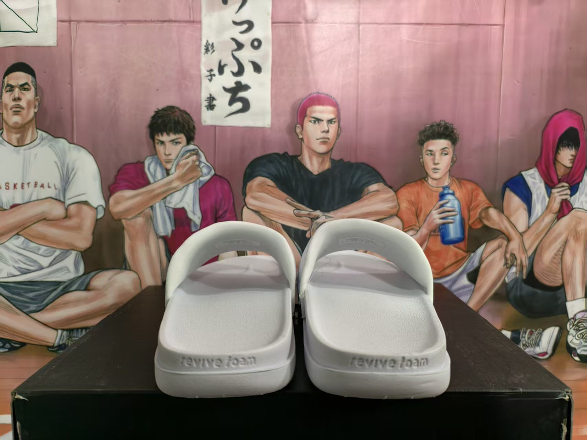 Pair of white Nike slides shown from the rear, with embossed “revive foam” wording on the heel area.