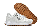 Pair of white Prada logo sneakers shown from the side and underside, highlighting the gum-colored tread.