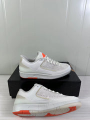 Side view of the sneaker pair showing the perforated forefoot panels, tonal laces, white midsole, and orange outsole sections.