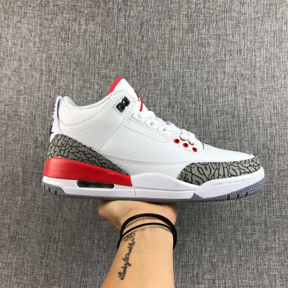 Side view of a white, red, and grey Jordan Air Jordan 3 sneaker