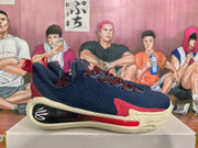 Side profile of a navy blue basketball sneaker with red accents, cream sole, and black-and-red heel detail.