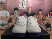 Front view of white Nike basketball sneakers with purple outsoles and yellow tongue accents.