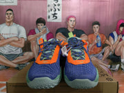 Front view showing the blue textured uppers, orange trim, multicolor laces, and green toe outsoles.
