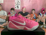 Side view of pink Nike basketball sneakers showing the contrasting swoosh, textured upper, layered heel panel, and pale outsole.