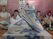 Angled view of the pair of white and blue Jordan 4-style sneakers displayed on a patterned box.