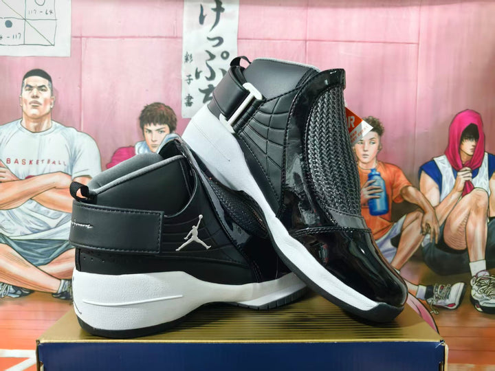 Black and white Jordan high-top sneakers shown from the side with a wide strap, woven-look panels, glossy overlays, and a white sole.
