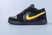 Side profile of a black low-top sneaker with a yellow side logo and black outsole.