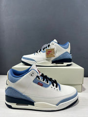 Side and front three-quarter view showing the white upper, blue panels, black laces, and red accents.