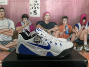 Side profile of a white and blue Nike sneaker showing the blue Swoosh, perforated side panel, speckled midsole, and black outsole.