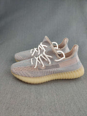 Pair of grey and pink-toned Yeezy 350 V2 style sneakers shown at a three-quarter angle on a grey surface.