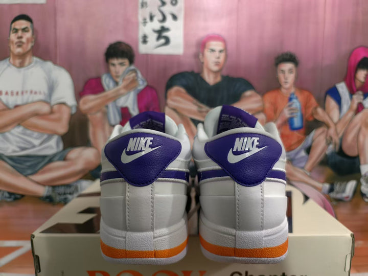 Rear view of white Nike sneakers with blue-purple heel tabs and orange outsole accents, displayed on a shoebox.