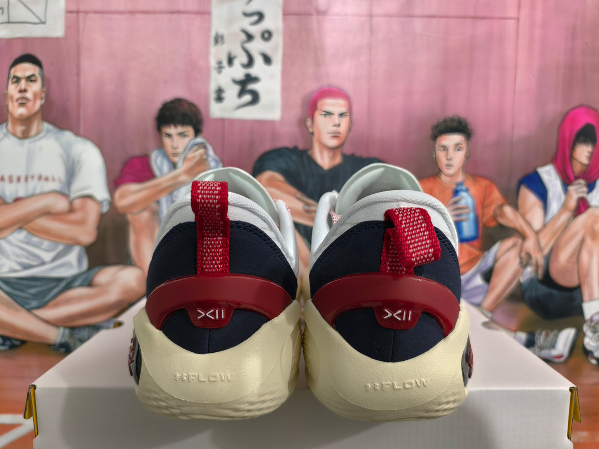 Rear view of white sneakers showing red heel pull tabs, dark navy heel panels, and cream-colored outsoles.