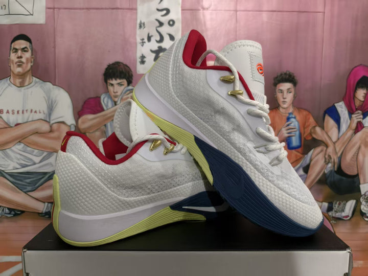 Pair of white Nike basketball sneakers with red lining, gold-toned lace hardware, and navy and lime-green outsole accents, shown on a box.