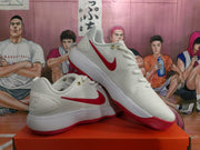 Angled view of a pair of white Nike sneakers showing the red Swoosh, white midsoles, and red outsole sections.