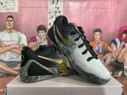 Angled view of GiGi sneakers with black and white uppers, gold side branding, and marbled gray outsole details.