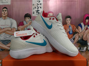Angled view of the pair of white Nike sneakers displaying the blue Swoosh, red accents, white laces, and ribbed outsoles.