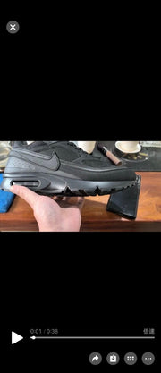Handheld side view of an all-black Nike sneaker with a Swoosh and heel Air unit.