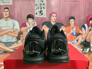 Rear view of black basketball sneakers showing glossy heel panels with light-colored signature-style markings and padded collars.