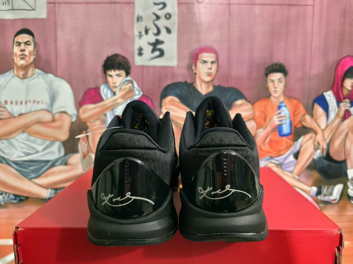 Rear view of black basketball sneakers showing glossy heel panels with light-colored signature-style markings and padded collars.