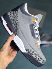 Side view of a grey sneaker with white laces, orange eyelets, and elephant-print panels