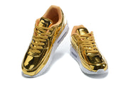 Pair of gold-tone Nike Air Max 90 QS sneakers shown from above.