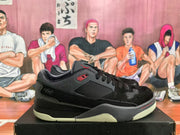 Side profile of a black and grey low-top sneaker showing mesh-like side paneling, red detailing, and a layered outsole.