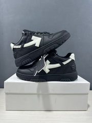 Two black and white sneakers stacked on a box, showing the contrasting arrow panels, heel construction, and attached product tag.