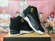 Pair of black high-top sneakers with gold hardware, textured black overlays, and white soles displayed on a box.
