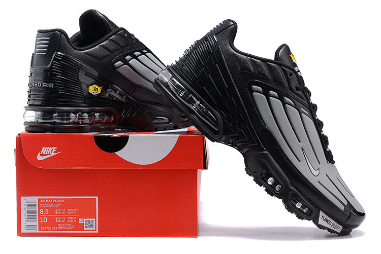 Black and grey Nike Air Max Plus sneakers displayed with a shoebox; the box label shows a sample size.