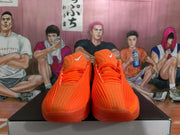 Front view of bright orange Nike sneakers showing the laces, padded tongues, textured uppers, and white Swoosh marks.