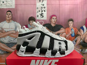 Side view of white, black, and grey Nike Air More Uptempo sneakers with oversized AIR lettering.