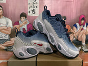 Angled side view of the Nike sneakers showing the red Swoosh, dark blue patterned upper, white overlays, and sculpted outsole.