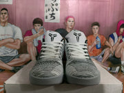 Front view showing the paired white and gray basketball sneakers, white laces, black accents, and Kobe-style tongue emblems.