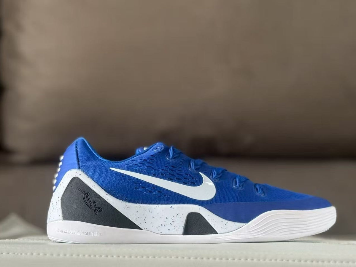 Side profile of a royal blue low-top sneaker with a white swoosh, black heel panel, and white speckled midsole.