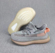 Gray and coral Yeezy 350 V2 kids' sneakers shown from the side with one sole facing upward.