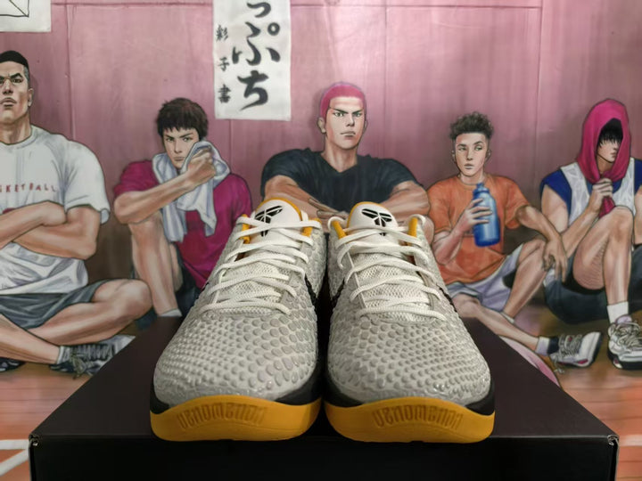 Front view of white, black, and gold Nike basketball sneakers displayed on a black box.