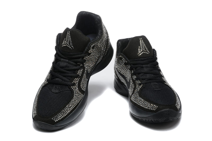 Pair of black Nike low-top sneakers shown from the front, with silver rhinestone-style detailing and contrasting tongue logos.