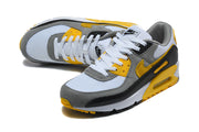 Angled top view of a pair of Nike Air Max 90 sneakers in white, grey, yellow, and black.
