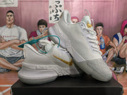 Angled view of white Nike basketball sneakers showing the gold swoosh, textured upper, layered sole, and teal accessory tag.