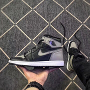 Side profile of the black and grey high-top sneaker held in a hand, showing the ankle emblem and white midsole.