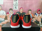 Rear view of red and black Nike sneakers with gold heel accents and white outsoles on a black shoebox.