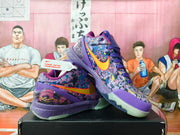 Pair of purple Nike basketball sneakers with multicolor graphic panels, orange swooshes, and translucent outsoles displayed on a black box.