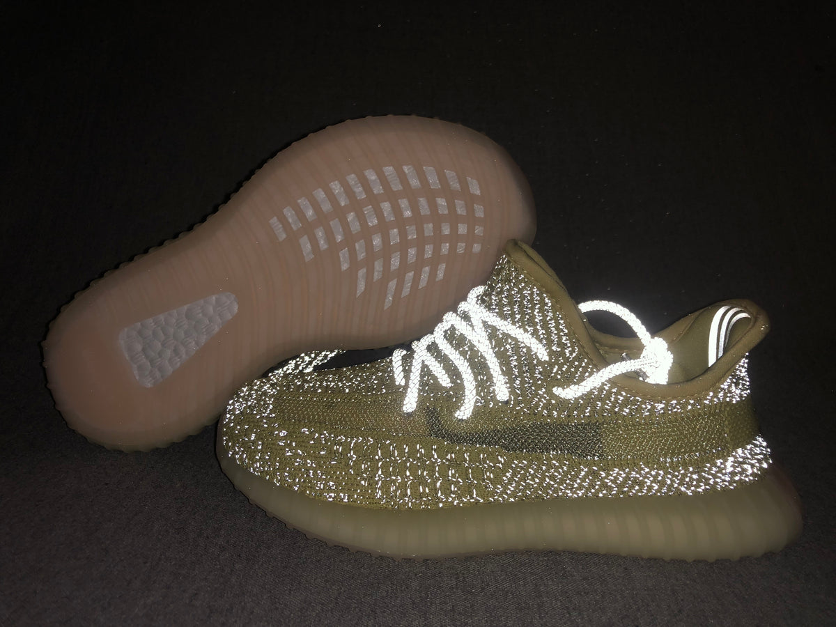 Pair of olive-yellow and black Yeezy 350 V2-style kids sneakers shown with the translucent outsole facing upward.